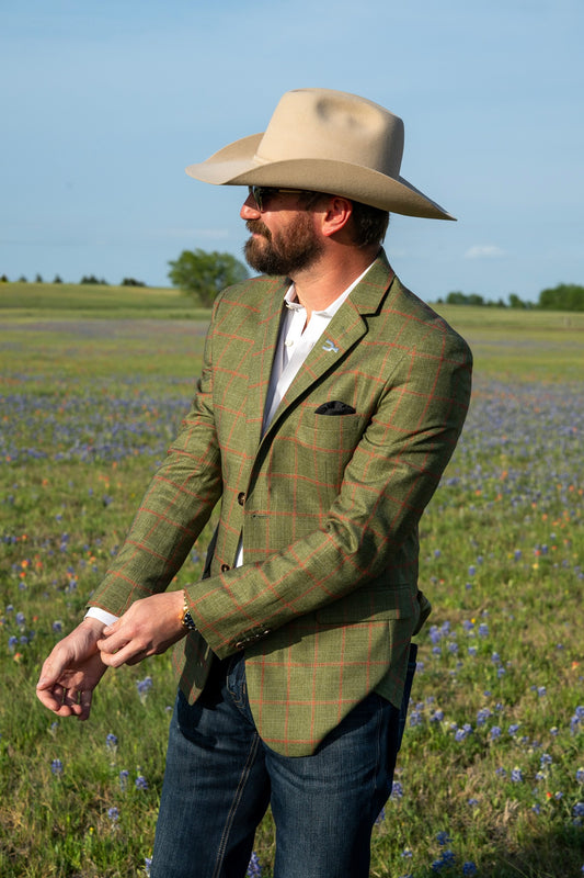 Man wearing a green plaid jacket and beige hat in a field with blue flowers