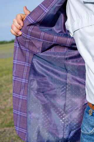 Person holding a purple plaid jacket with a reflective surface against a grassy background