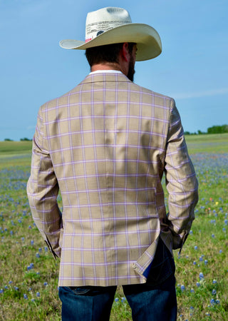 Man wearing a beige checkered jacket and cowboy hat in a field with blue sky.