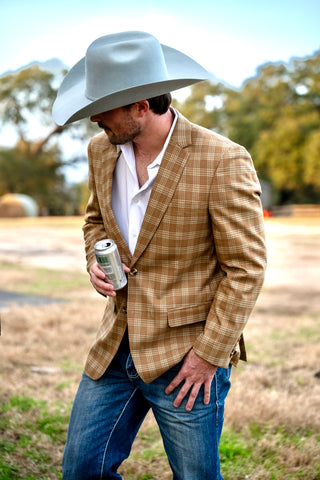 Man wearing a plaid jacket, jeans, and a cowboy hat holding a can in an outdoor setting.