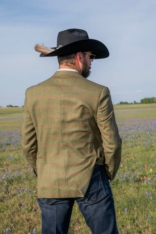 Man wearing a green checkered jacket and black cowboy hat standing in a field with wildflowers.