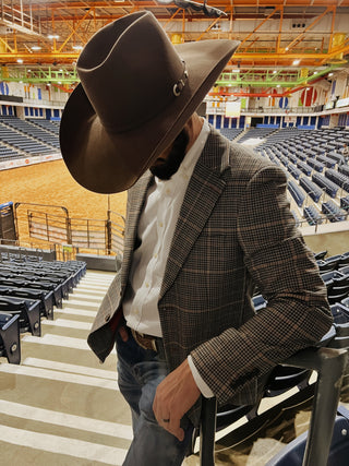Man wearing plaid cowboy sport coat and black cowboy hat overlooking WRCA World Championship Ranch Rodeo arena in Amarillo Texas featuring western formalwear by Espuela Design Co.