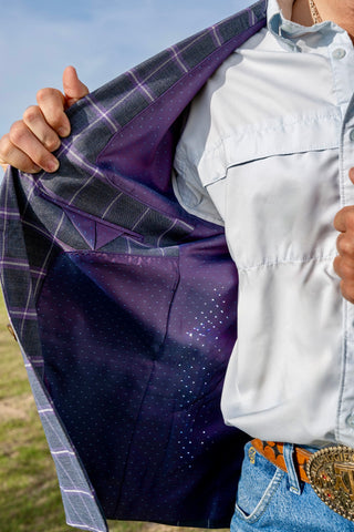 Person wearing a white shirt and blue jeans with a purple jacket open, standing outdoors.