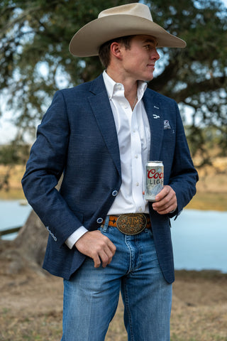 Man in cowboy hat and blue blazer holding a Coors Light beer by a body of water.