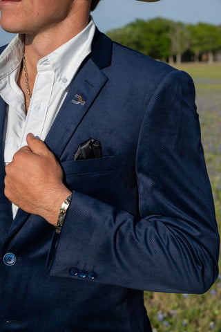 Man wearing a navy blazer with a white shirt and a field in the background