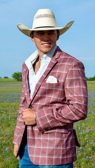 Man wearing a plaid jacket and cowboy hat in an outdoor setting with blue sky and green grass.