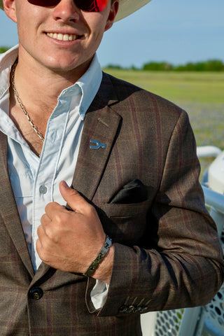 Man wearing a brown suit with a white shirt and sunglasses, standing outdoors.