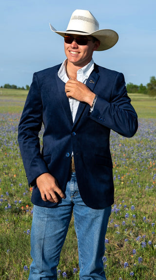 Man wearing a navy blazer, white shirt, and cowboy hat standing in a field with wildflowers.