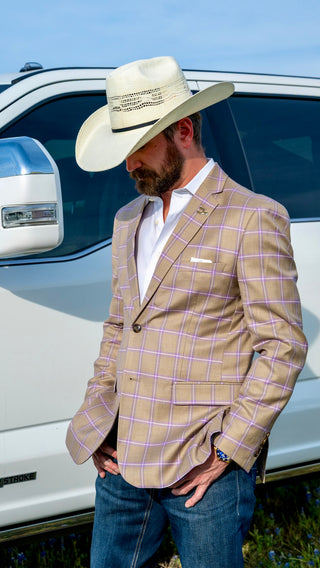 Man wearing a beige checkered blazer, white shirt, and blue jeans with a cowboy hat in front of a white truck.