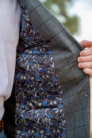 Close-up of a gray suit jacket with a floral pocket square and a blurred outdoor background.