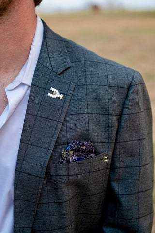 Gray checkered suit jacket with a pocket square and lapel pin, blurred background. Built for cowboys. Spur Lapel Pin