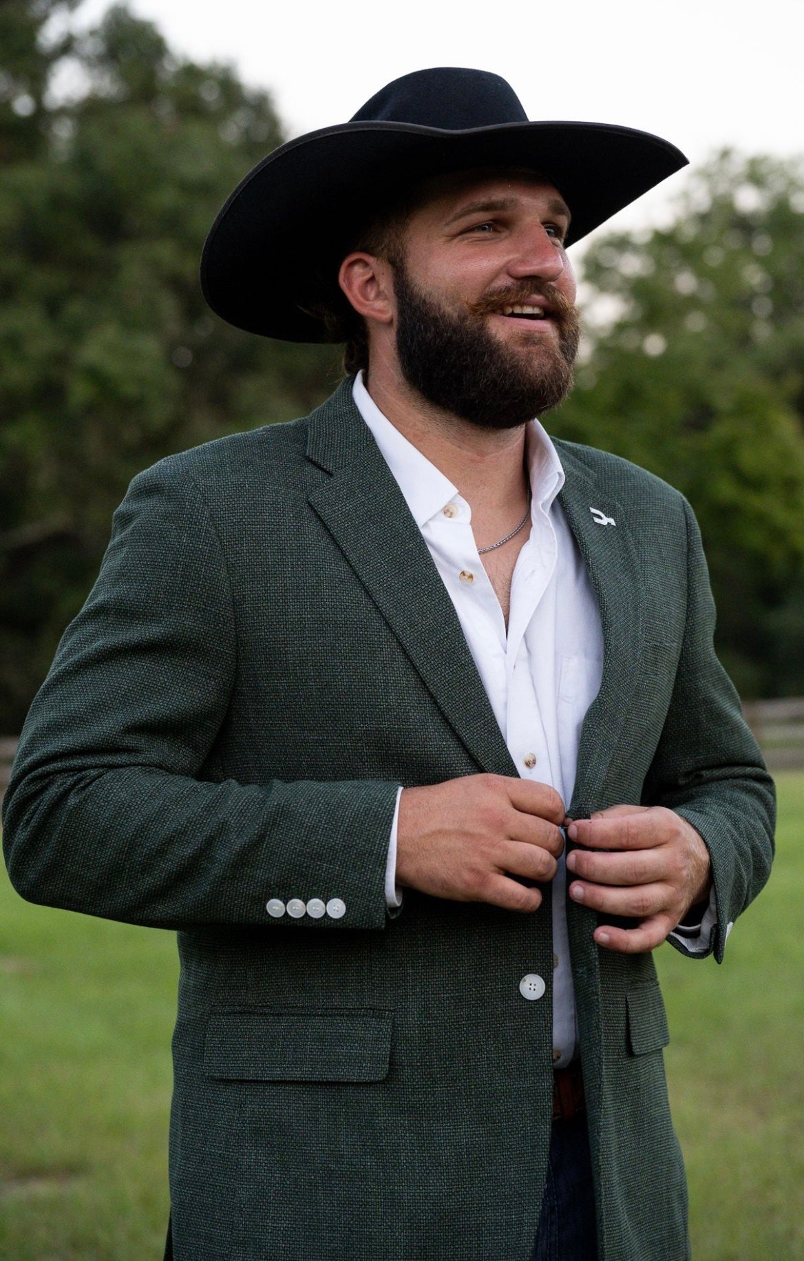 Man wearing a green suit and black cowboy hat outdoors