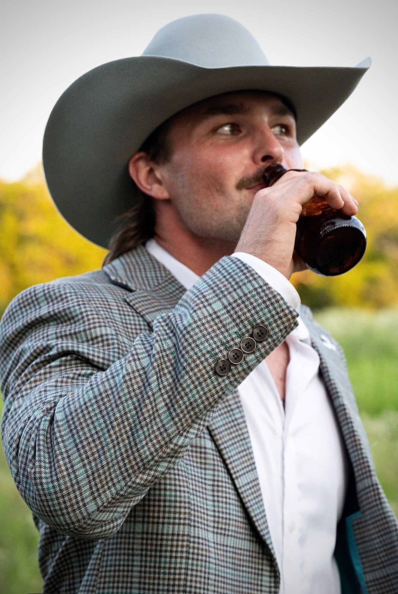 Man in cowboy hat and suit drinking from a bottle outdoors