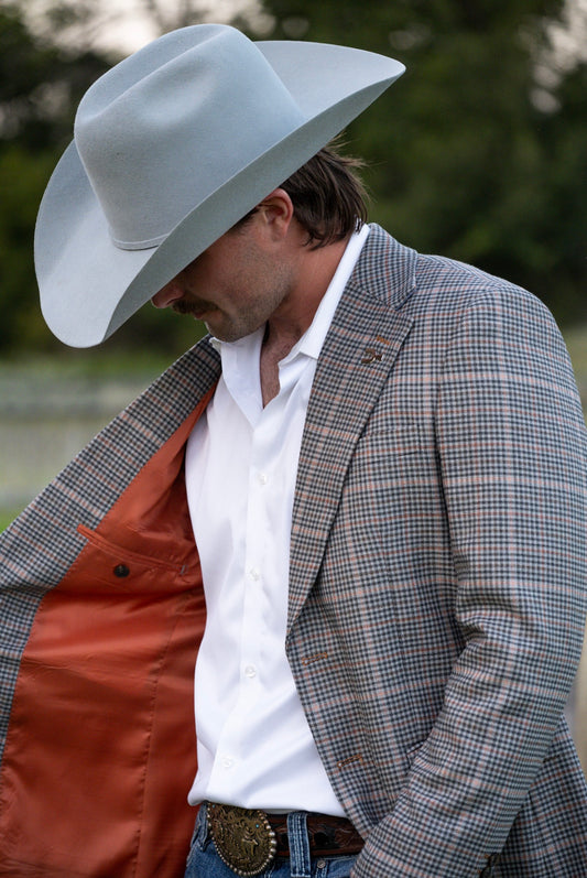 Man wearing a gray cowboy hat, plaid jacket, and white shirt outdoors.
